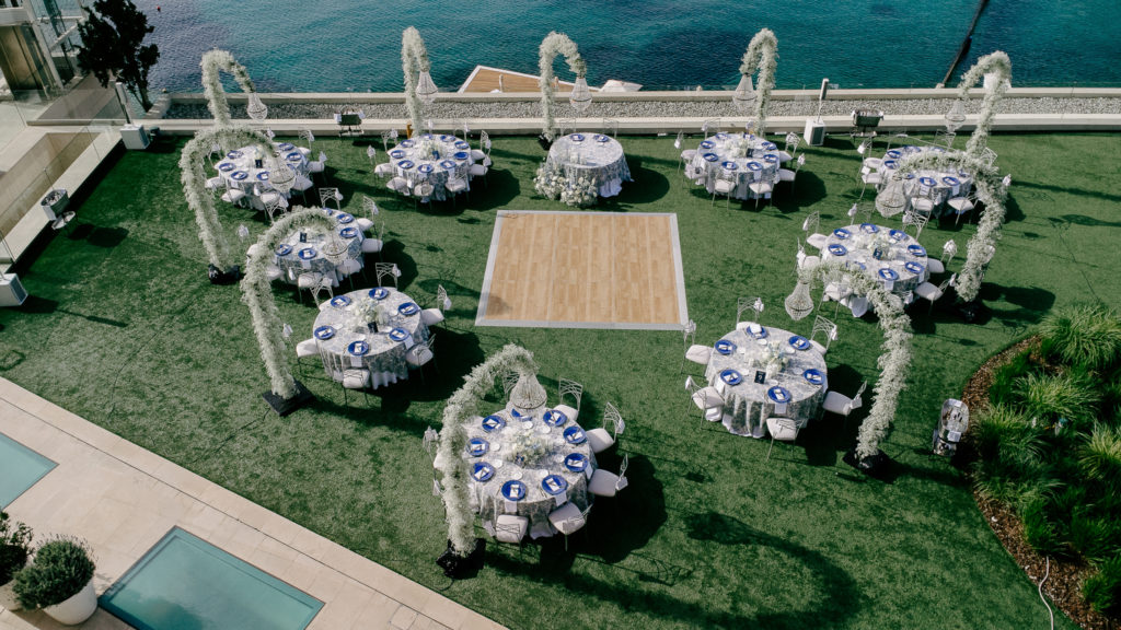 Aerial view of a seaside wedding reception in Athens featuring round tables, white floral arches, and seafront dining.