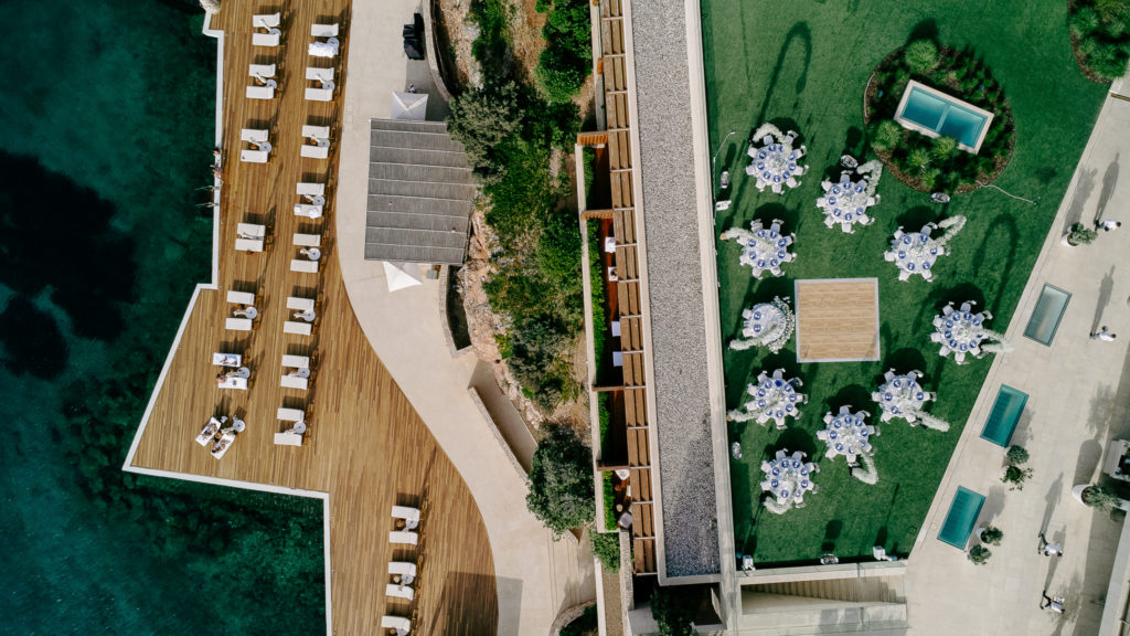 Drone view of a luxury seaside wedding venue in Greece showing dining area, dancing floor, and waterfront lounge deck