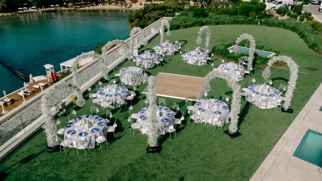 Aerial view of a seaside wedding reception in Athens featuring round tables, white floral arches, and seafront dining.