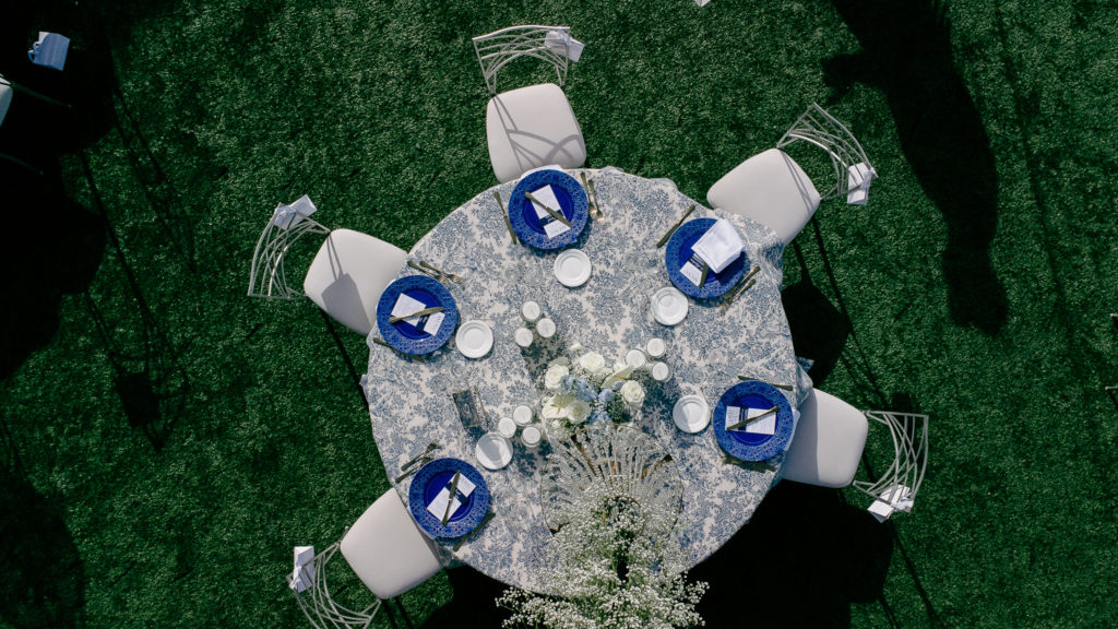 Close-up of a wedding reception table in Athens with blue patterned charger, printed menu, candles, and gold cutlery.