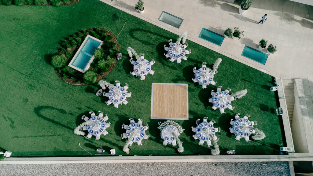 Aerial view of a seaside wedding reception in Athens featuring round tables, white floral arches, and seafront dining.