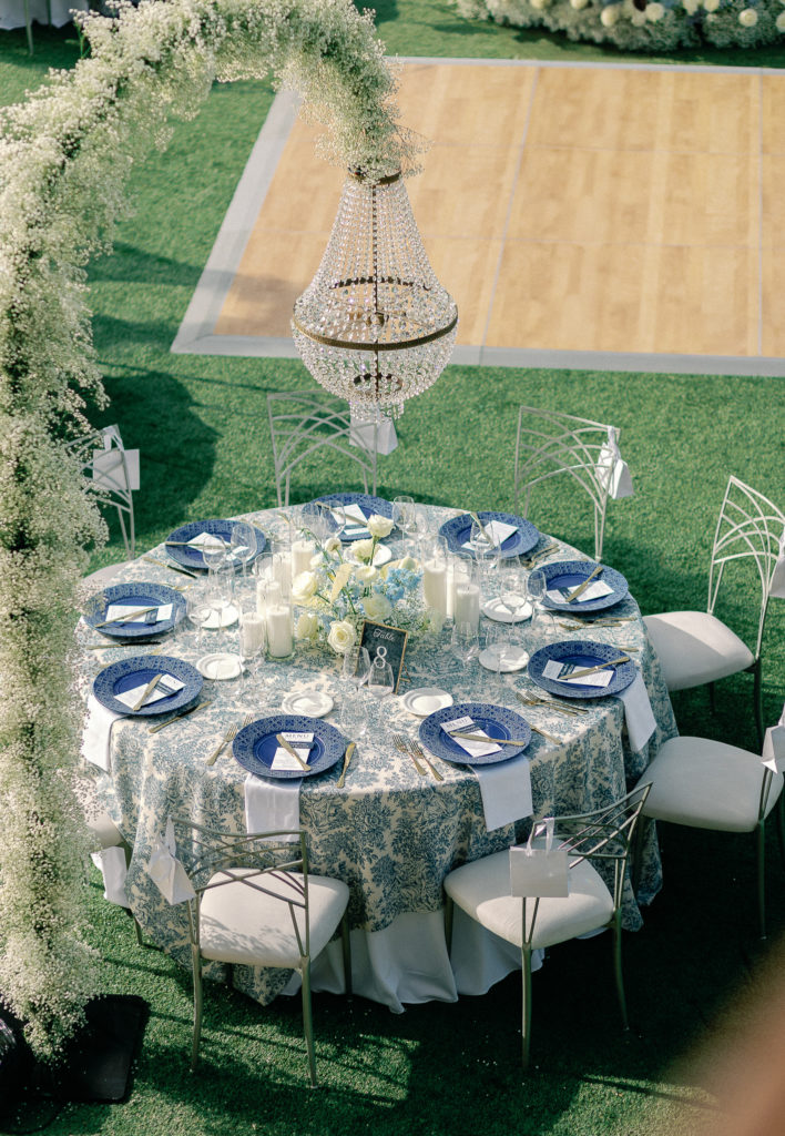Close-up of a wedding reception table in Athens with blue patterned charger, printed menu, candles, and gold cutlery.