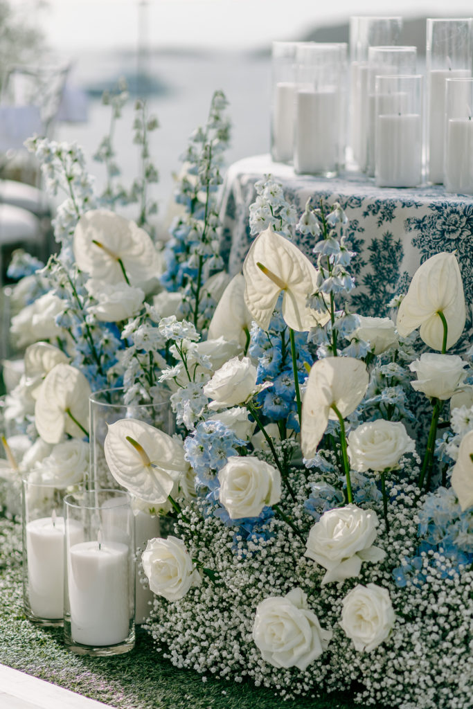 Bride and groom seated at candlelit sweetheart table under a floral chandelier with the sea in the background at a destination wedding in Greece - Decor