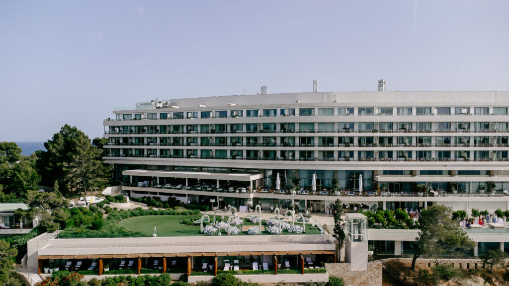 Drone view of a luxury seaside wedding venue in Greece showing dining area, dancing floor, and waterfront lounge deck