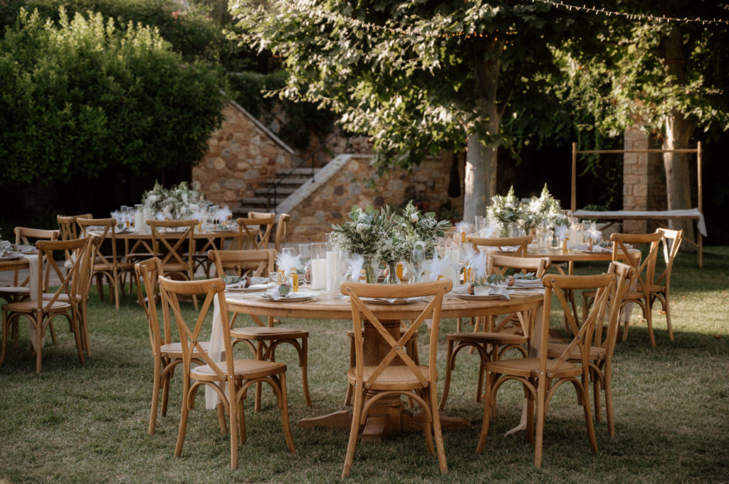 Wedding reception setup in castle courtyard with wooden tables, neutral linens and vineyard views