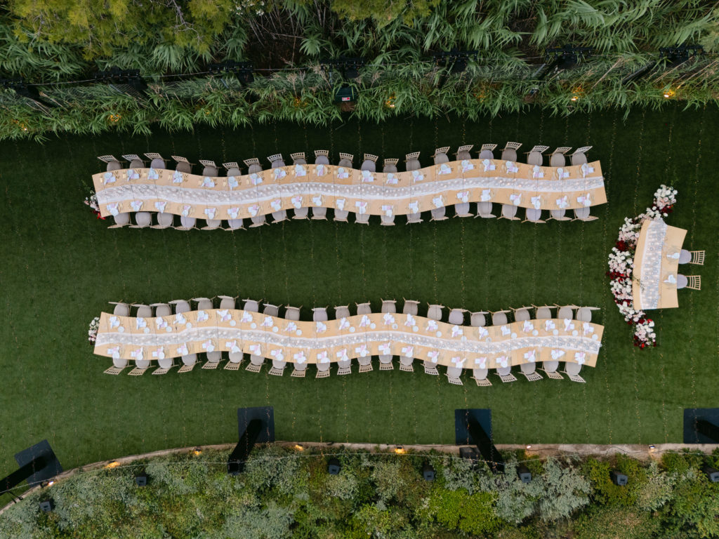 Drone view of cliffside seaview wedding reception setup in the Athens Riviera with long curved tables and coastal rocks below.