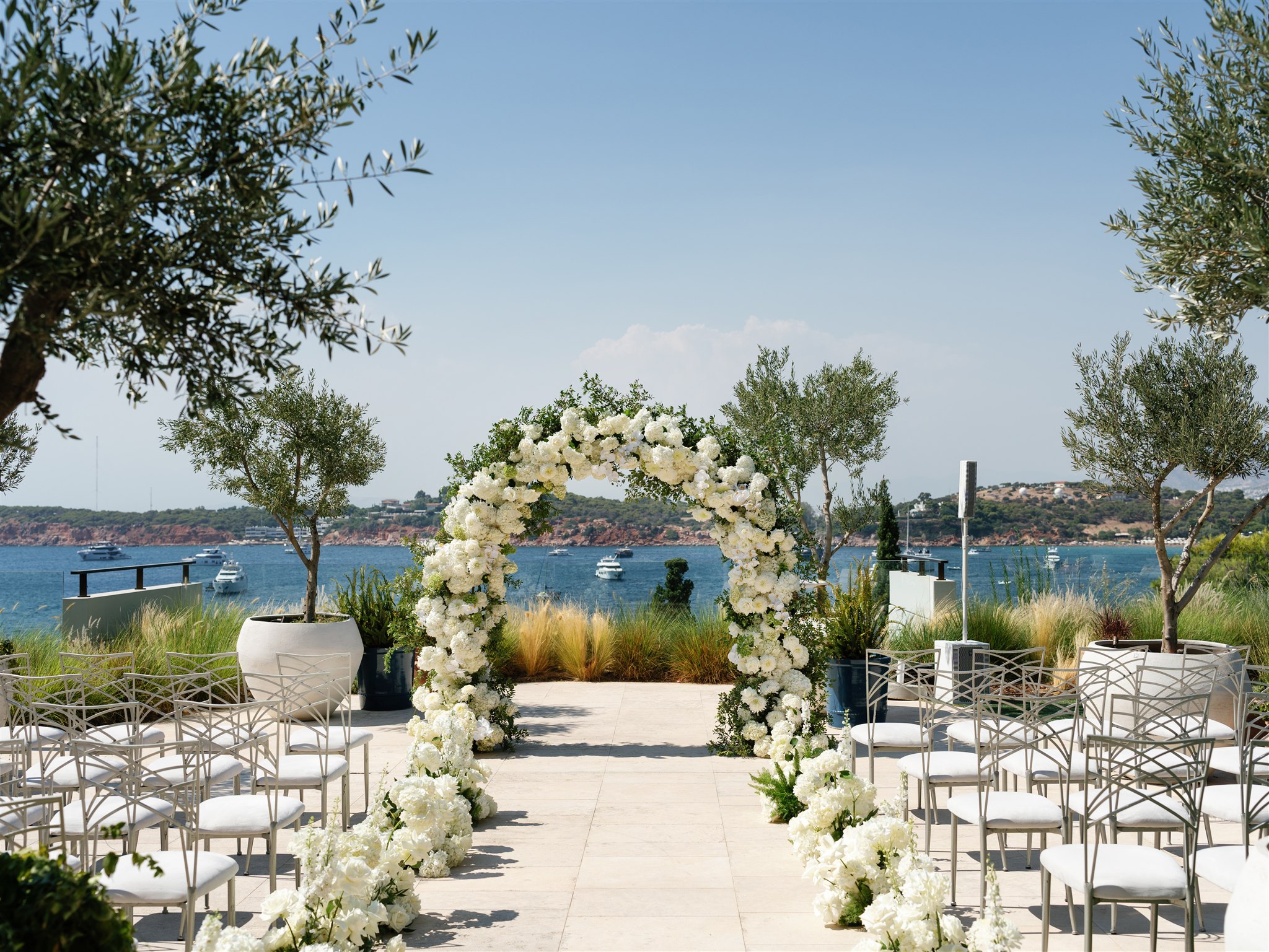 Luxurious white floral wedding arch and aisle setup overlooking the sea at Four Seasons Athens Riviera.