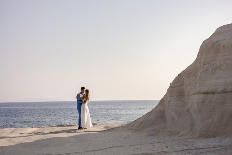 Bride and groom embracing on a sunlit cliff overlooking the Aegean Sea at a Romantic Cliffside Wedding in Milos