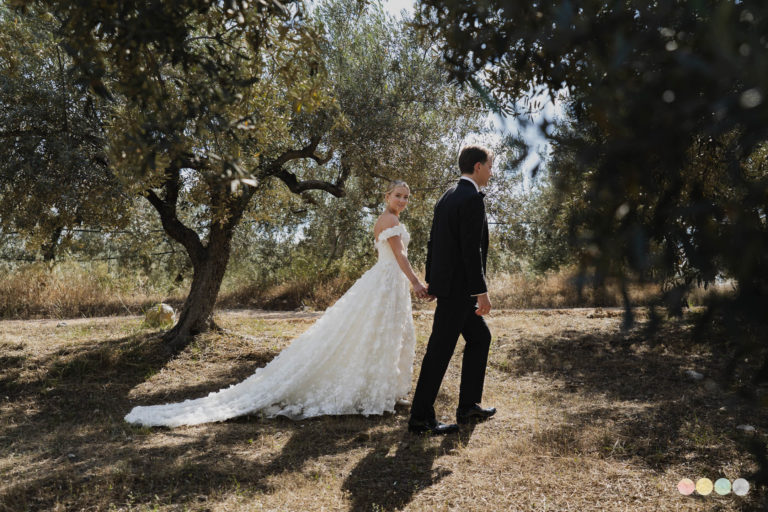 Bride in floral gown and groom in tux walking hand-in-hand through an olive grove after their Olive Grove Wedding in Nafplio
