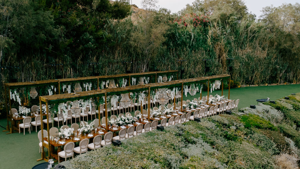 Overhead view of elegant wooden reception tables decorated with white flowers, gold chargers, and crystal elements