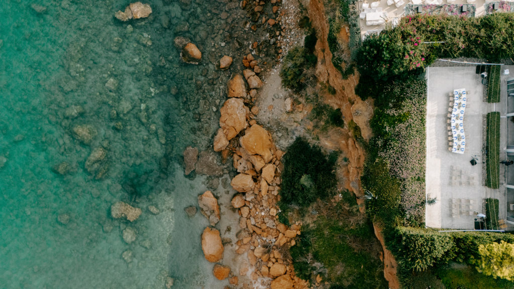 Overhead view of an intimate cliffside wedding dinner with blue charger plates and string lights in the Athens Riviera.