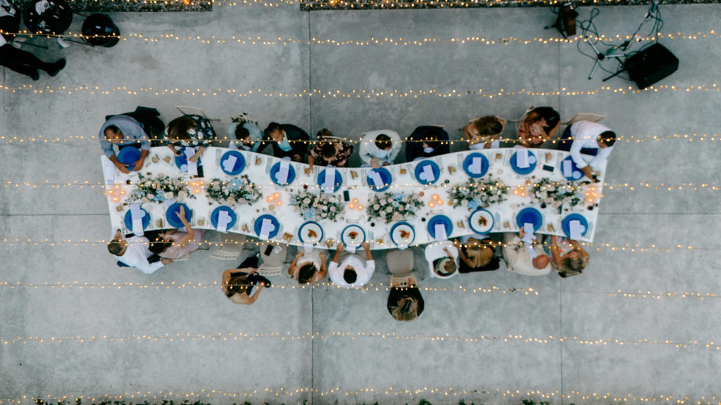 Overhead view of an intimate cliffside wedding dinner with blue charger plates and string lights in the Athens Riviera.